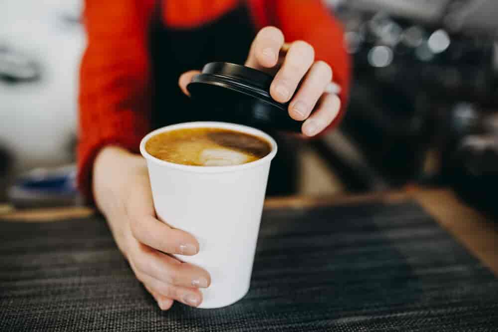 Barista holding hot cappuccino in white takeaway paper cup